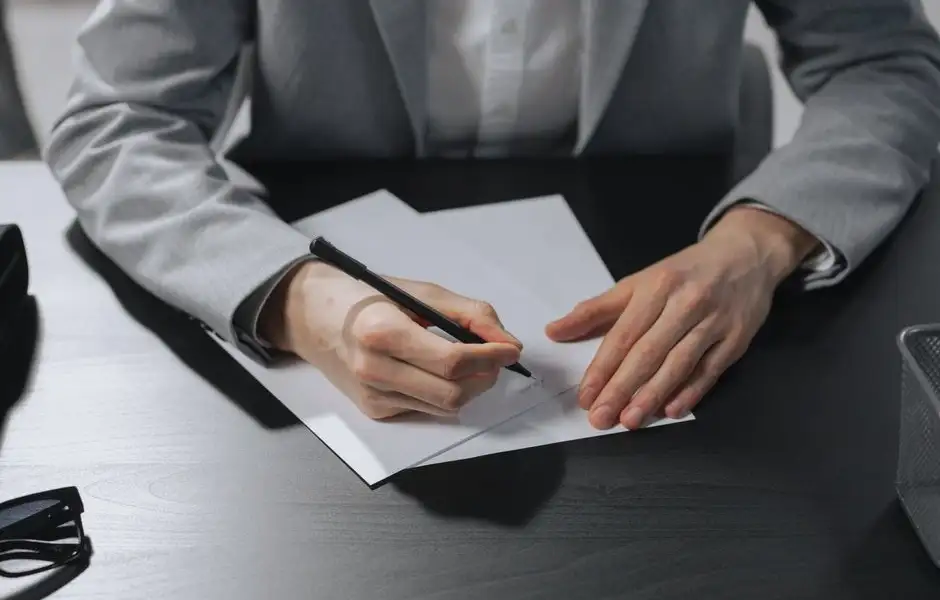 Une conductrice rédige une lettre de résiliation d’assurance auto, enveloppe et stylo sur le bureau.